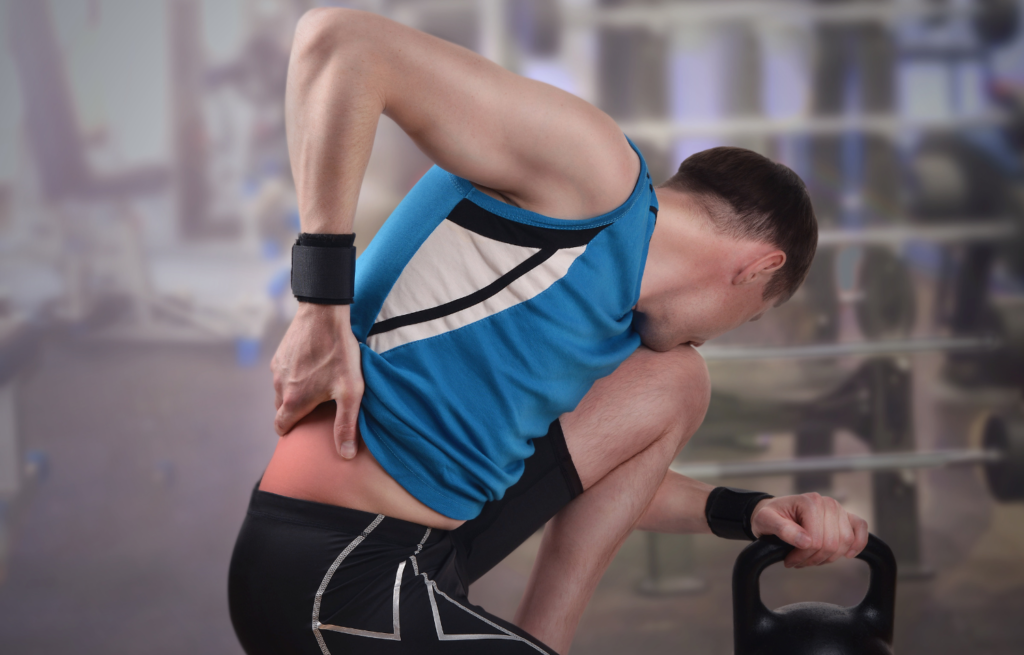 Man kneeling on one knee, grasping his lower back in discomfort at the gym.