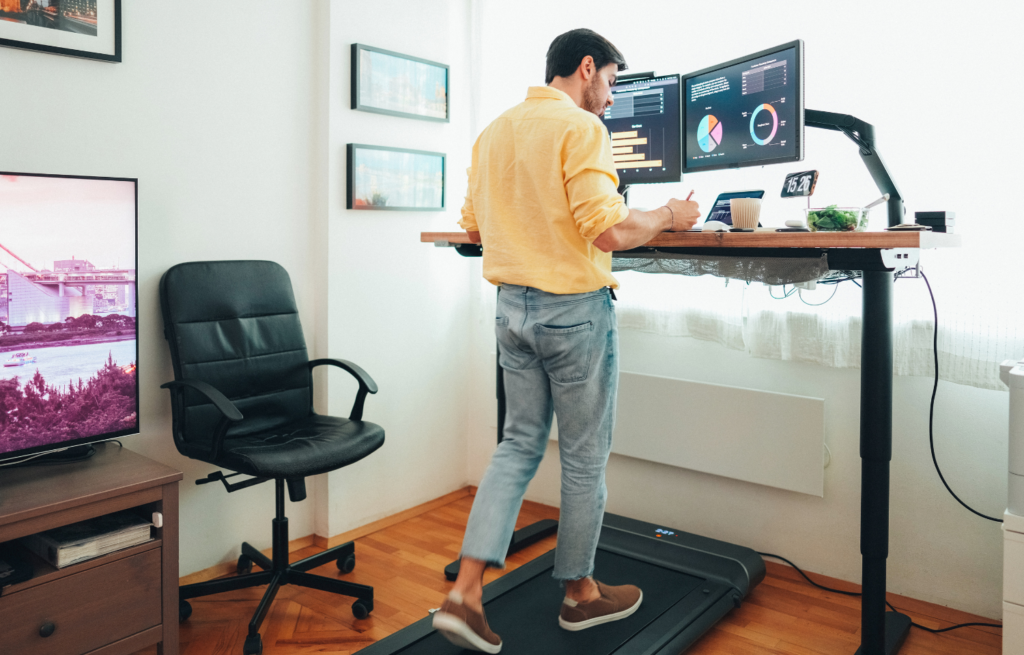 Man walking on a small treadmill designed for hi-lo desk work while using a computer.